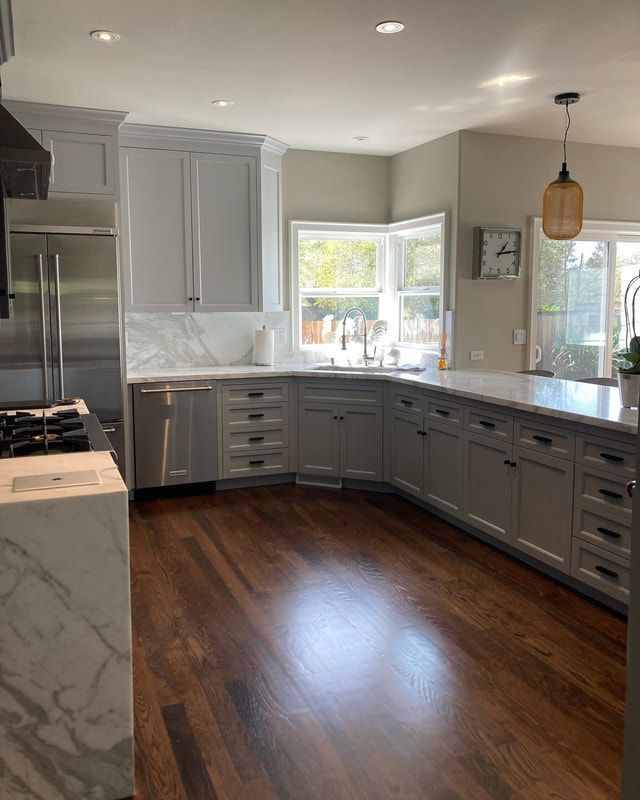 Gray and white kitchen with dark wood floors, featuring cabinets, countertops, stainless steel appliances, and a corner window.