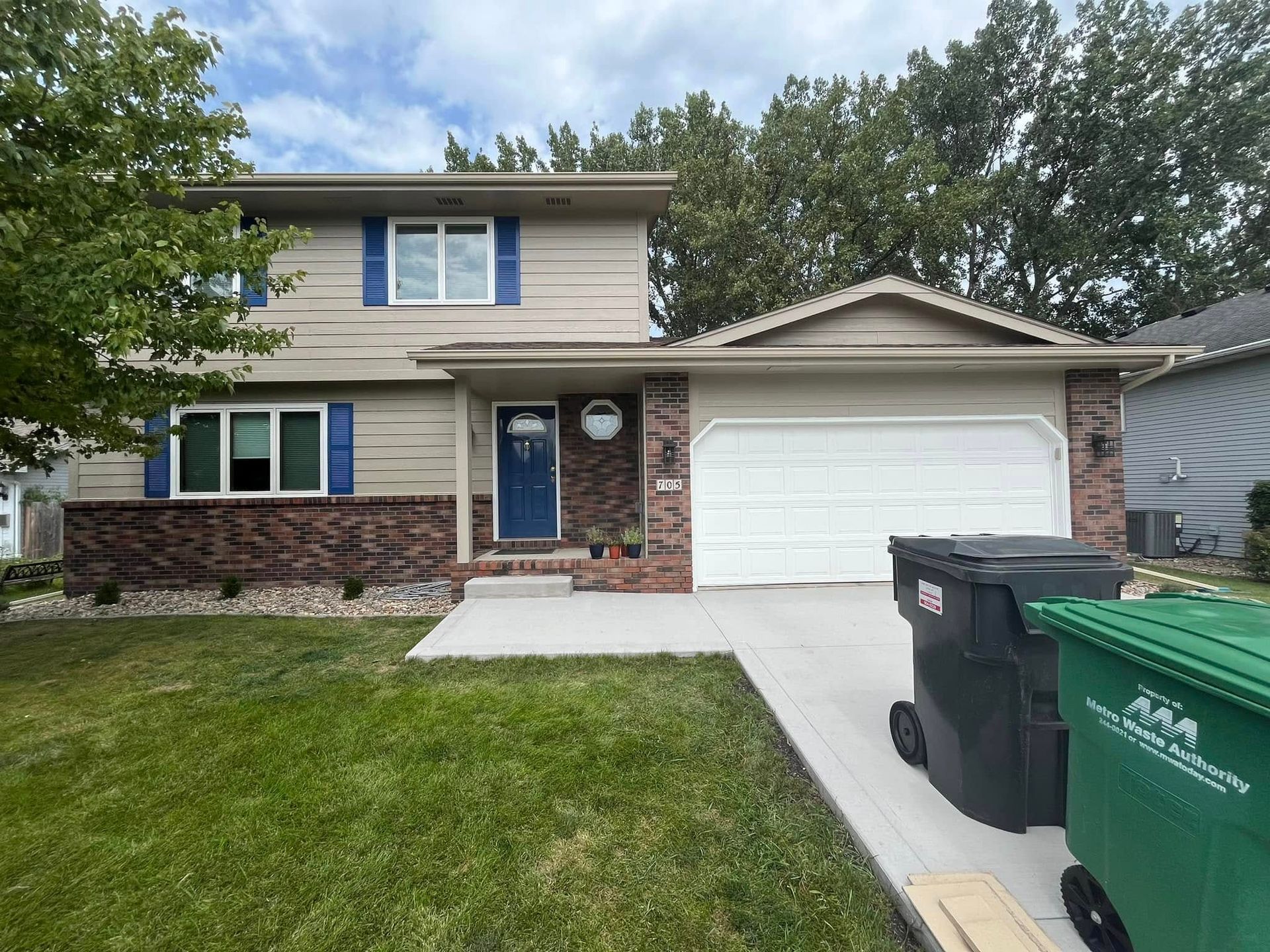 Two-story house with brick and tan siding, blue shutters, a blue front door, and a white garage door.