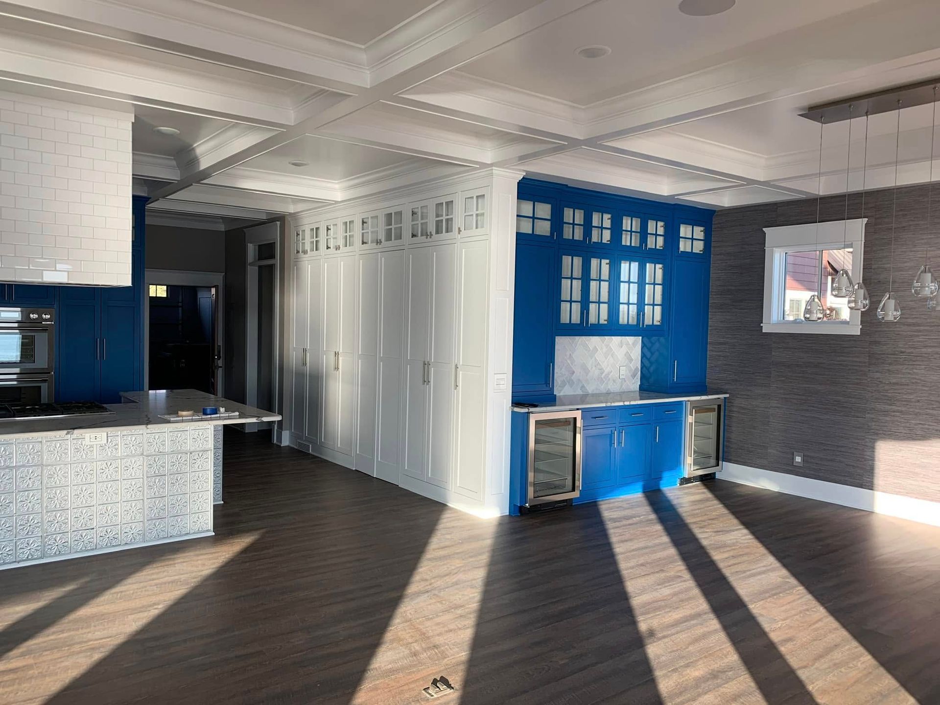 Empty room with blue cabinets, white paneling, and sunlight casting long shadows across a dark wood floor