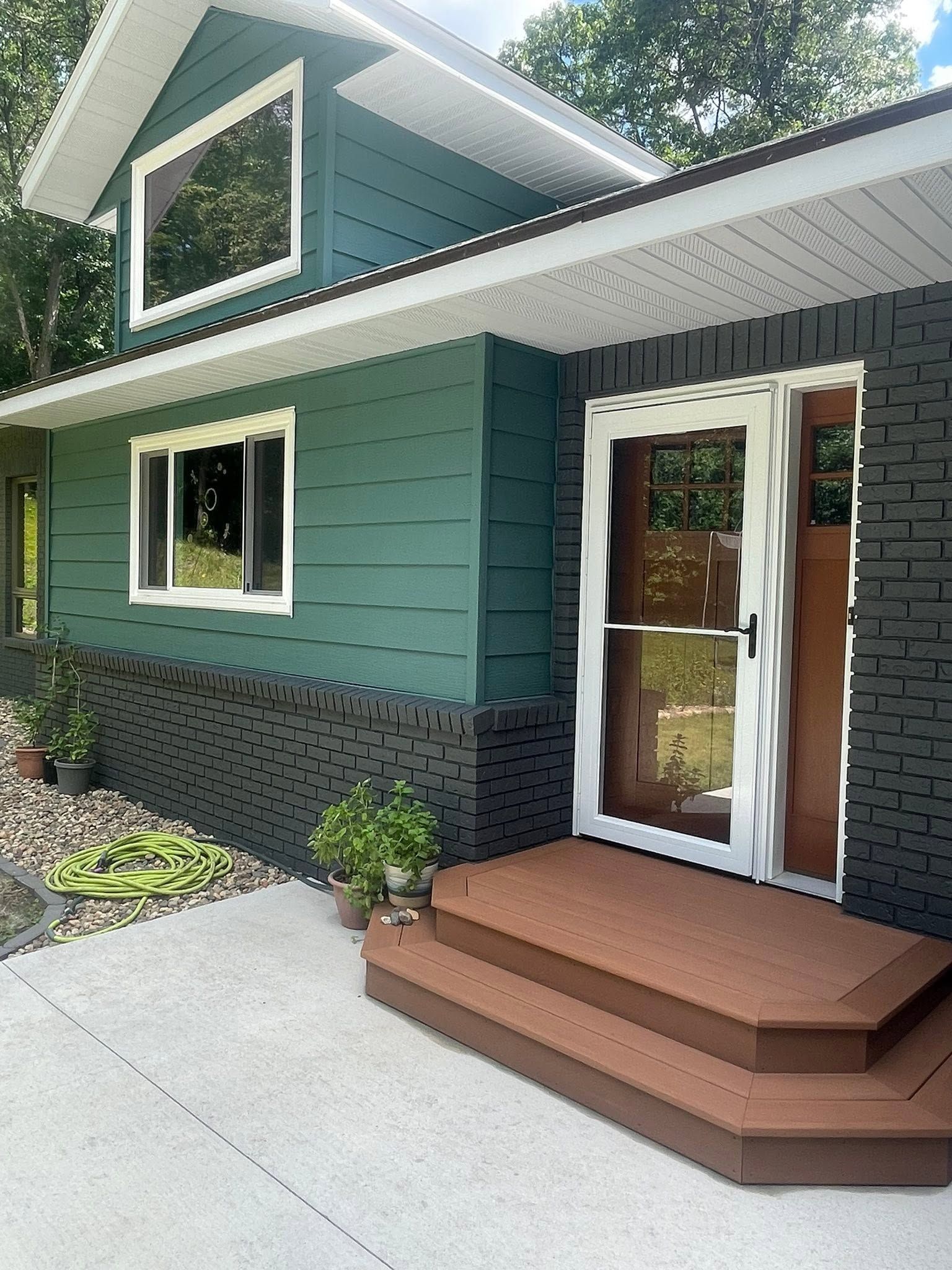 Teal house exterior with white trim, black skirting, and a small brown front porch by a concrete walkway