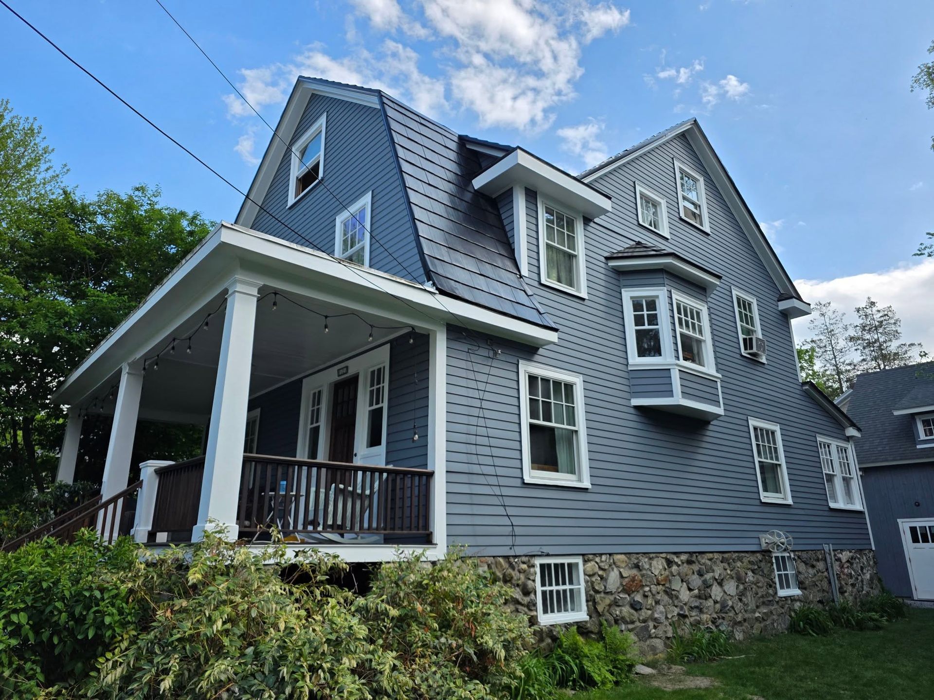 Gray Victorian-style house with stone foundation and covered porch under a blue sky