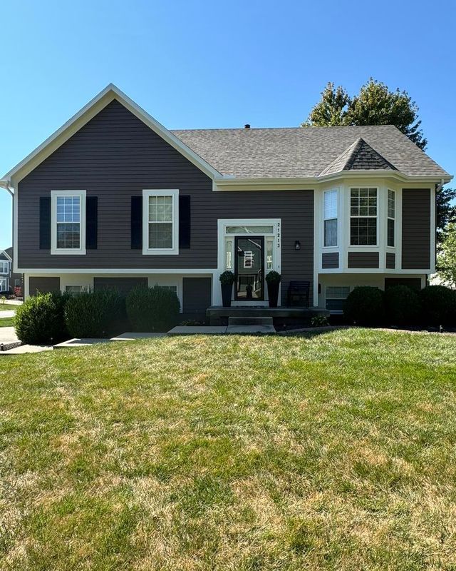 Gray house with white trim and a front porch, viewed from a green lawn under a clear blue sky
