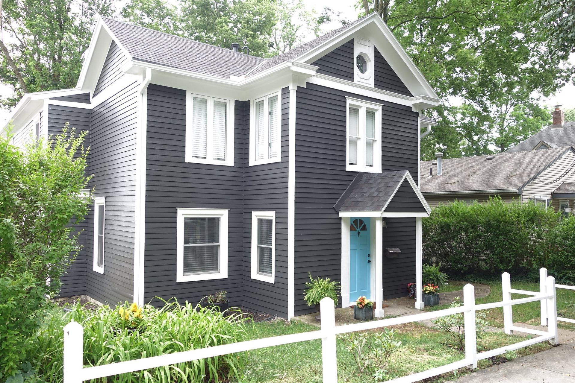 Dark blue two-story house with white trim and blue front door behind a white fence