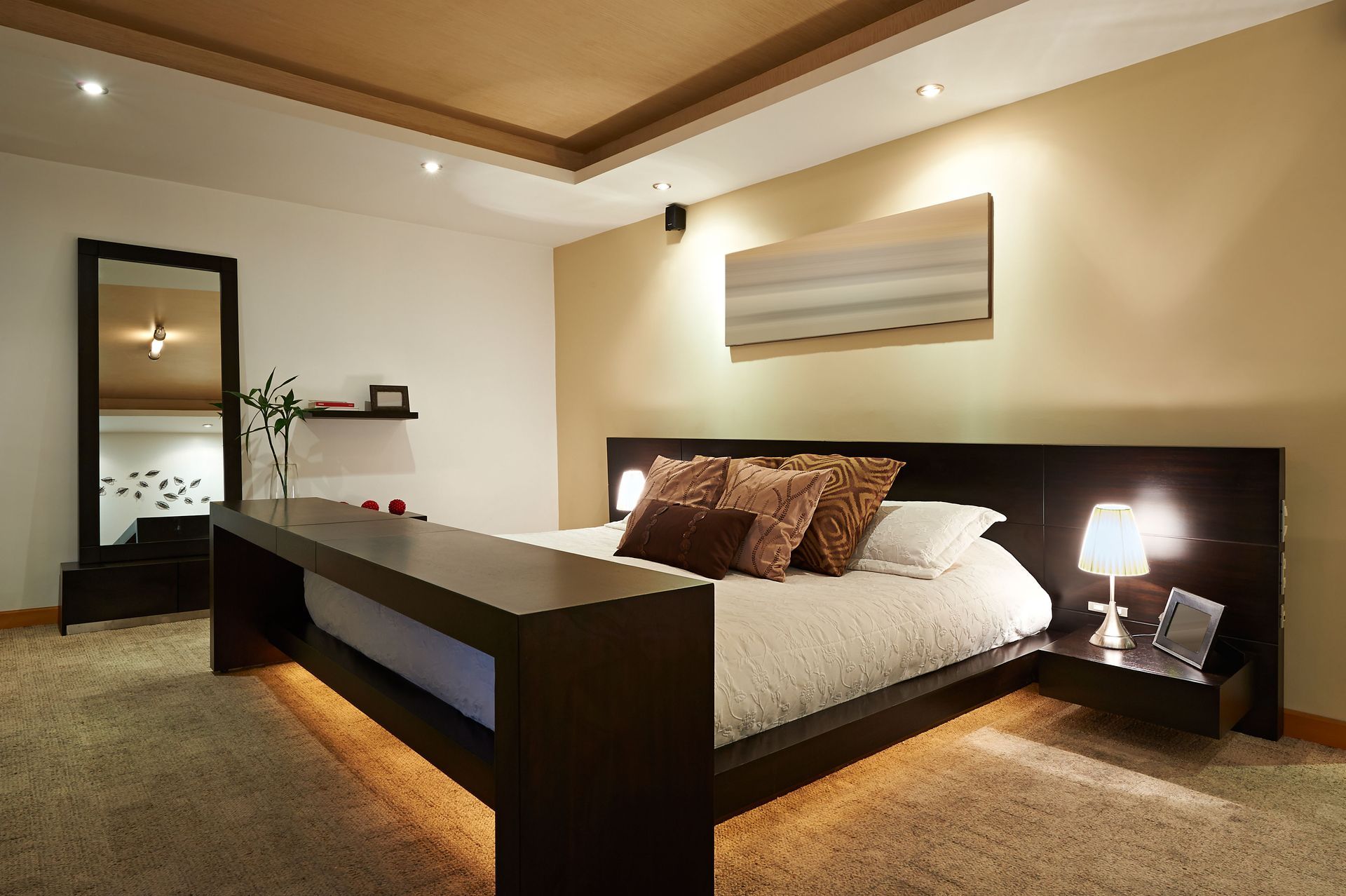 Modern bedroom with large bed, brown furniture, beige walls, and ambient lighting.