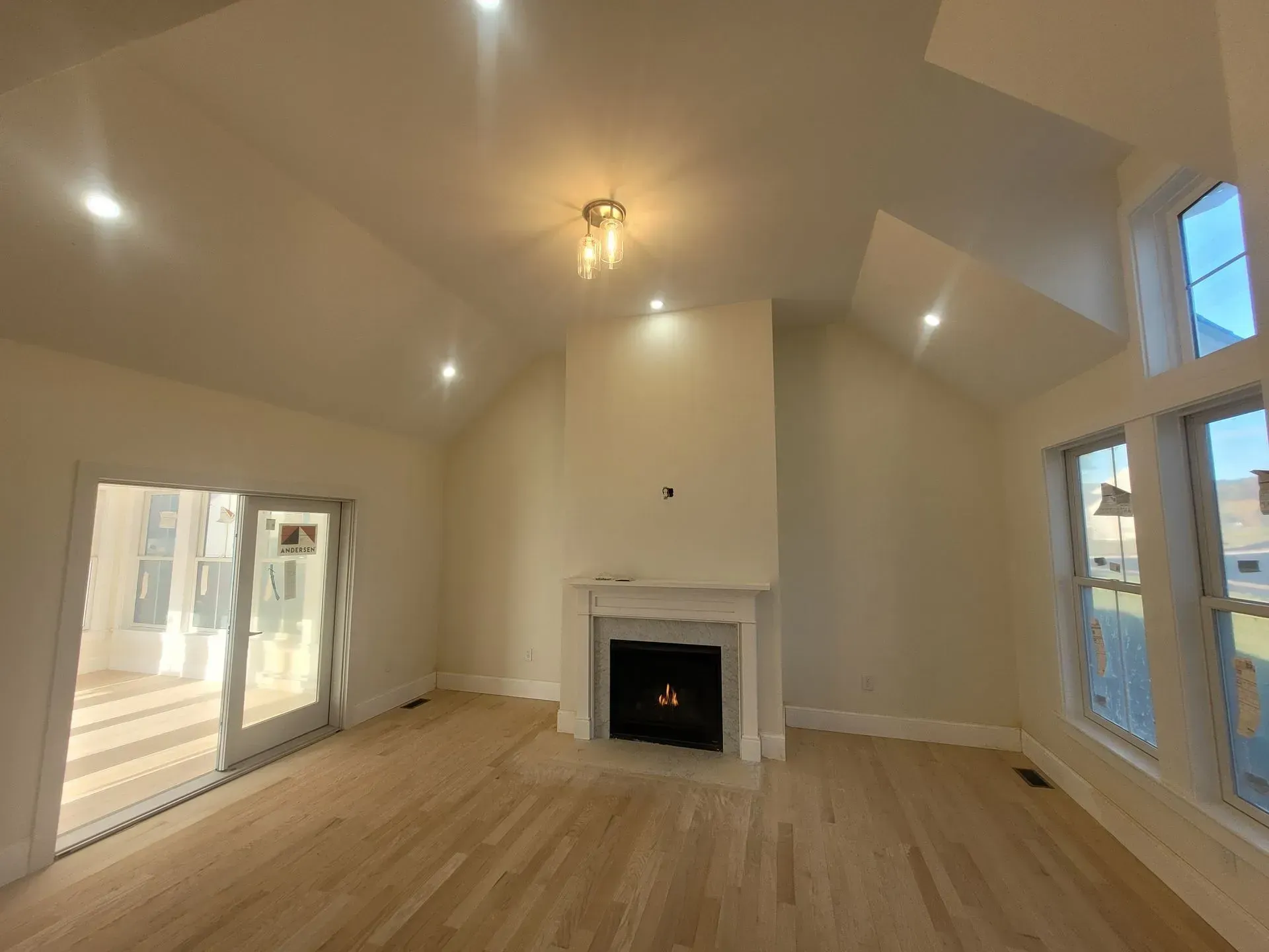 Light-filled living room with fireplace, vaulted ceiling, and sliding glass door. Blond hardwood floors, beige walls.