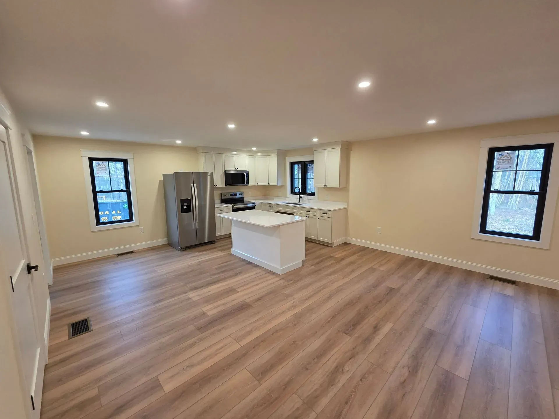 Open-concept kitchen and living area with white cabinets, stainless steel refrigerator, and wood-look flooring.
