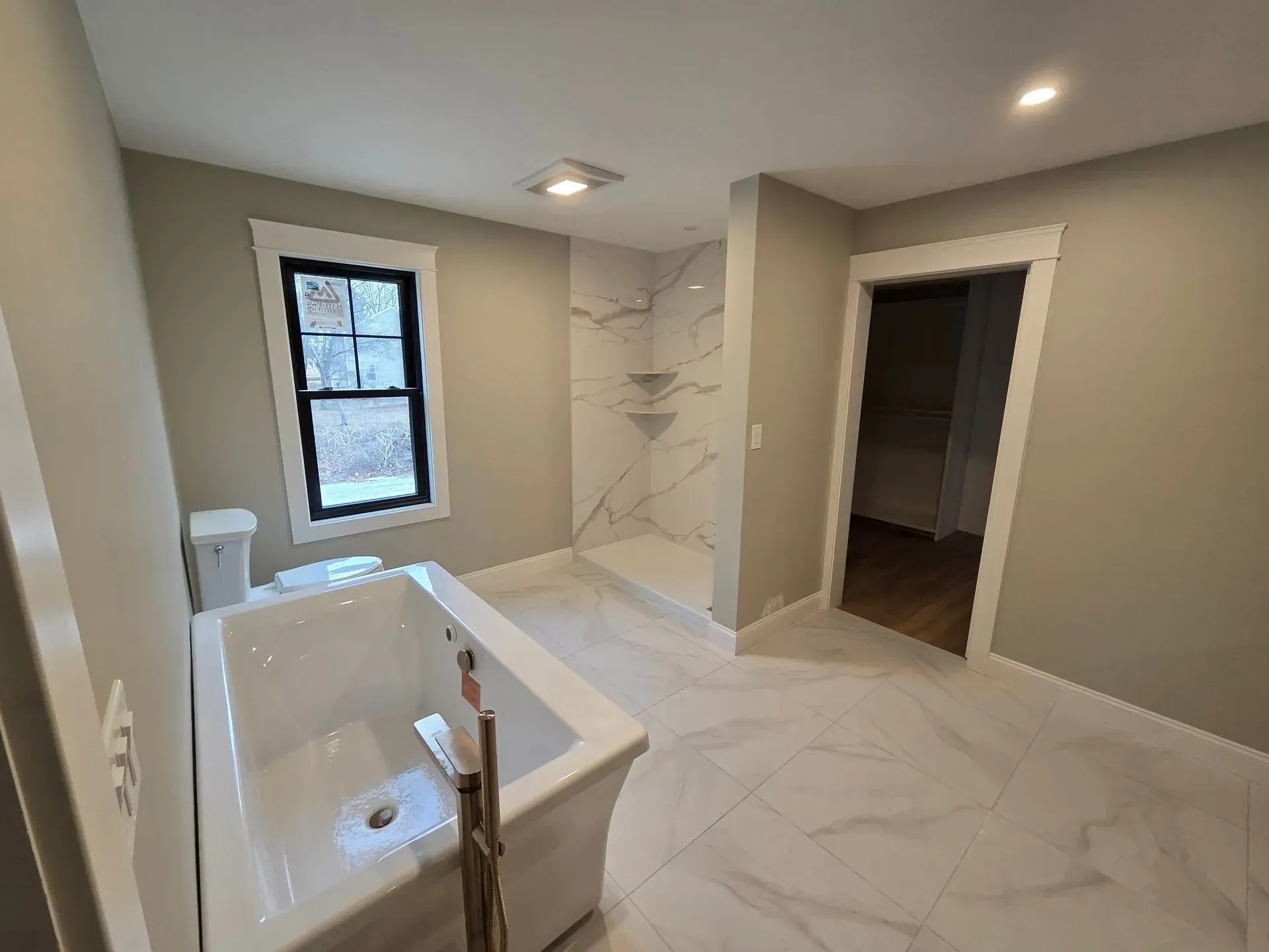 Newly renovated bathroom with a white tub, walk-in shower, and marble tile floor.