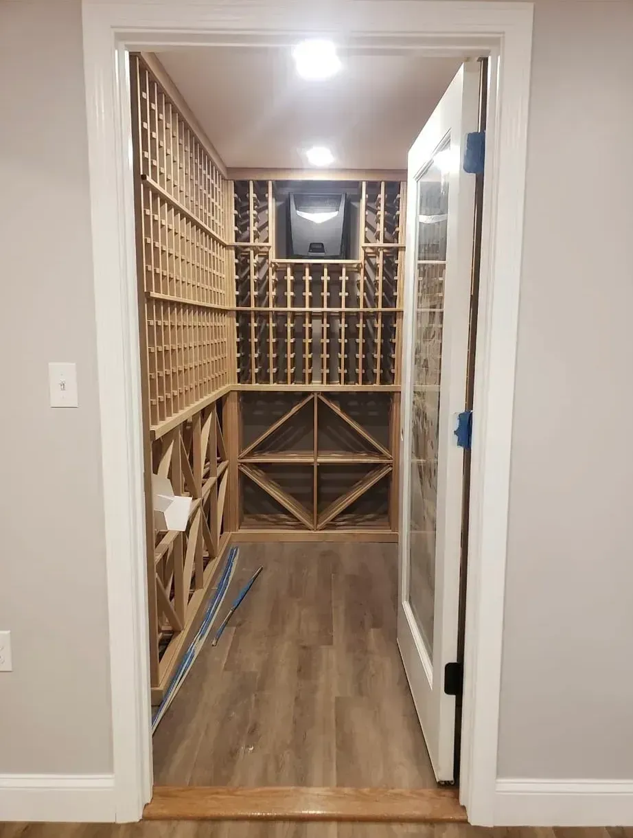 Wine cellar interior with wooden racks, door ajar, and gray walls.