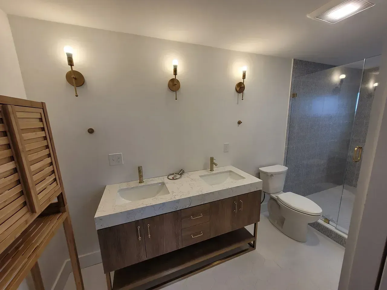 Bathroom with double vanity, gold sconces, and a walk-in shower.