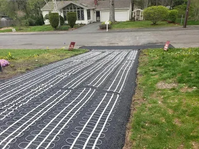 Driveway with white heating cables installed, prepared for paving. Green grass borders the driveway.
