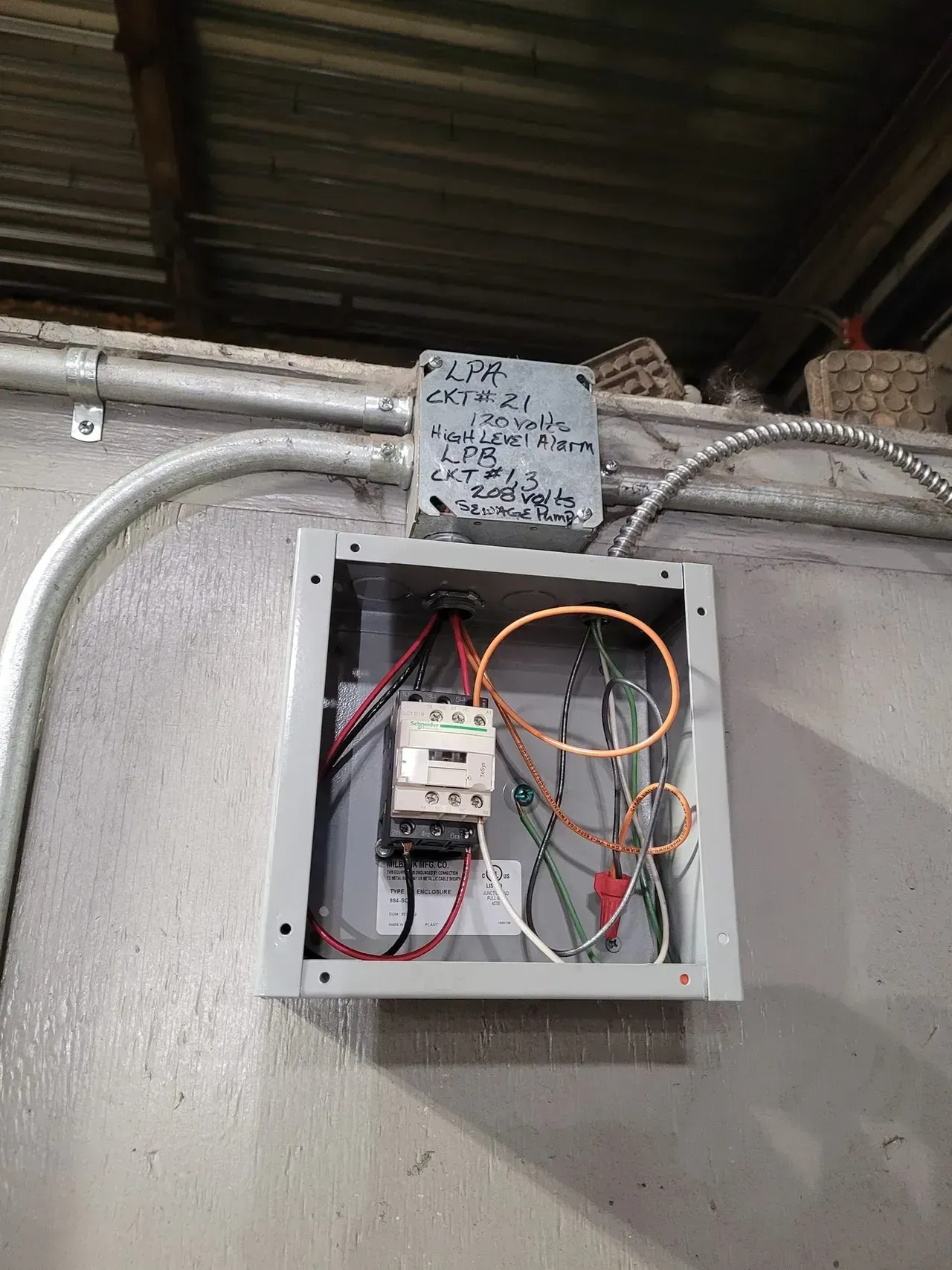 Electrical control panel mounted on a wall with conduit and wiring visible inside.