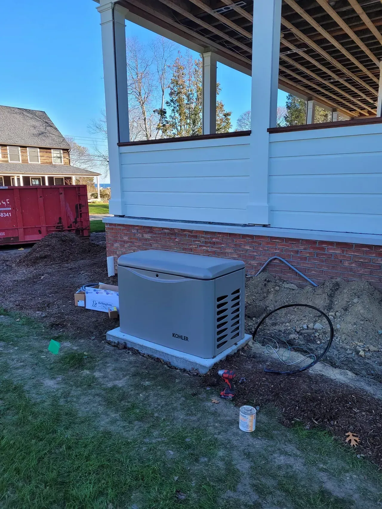 A beige generator on a concrete pad near a brick foundation. The structure has a white facade under a blue sky.