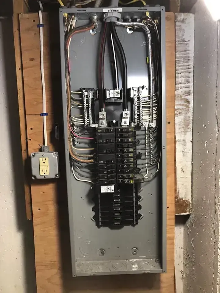 Electrical panel with circuit breakers, wires, and an outlet on a wooden surface.