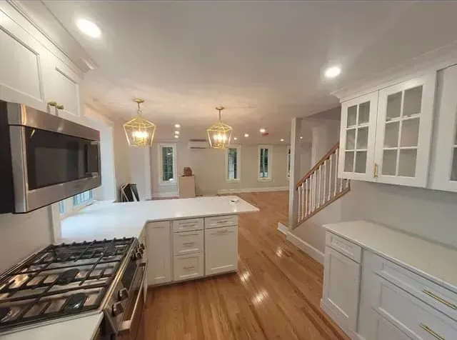 Modern kitchen with white cabinets, stainless steel appliances, wood floors, and pendant lights.