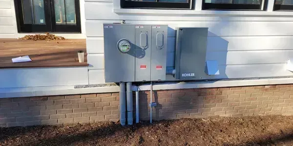 Gray electrical panel attached to a white house with conduits.
