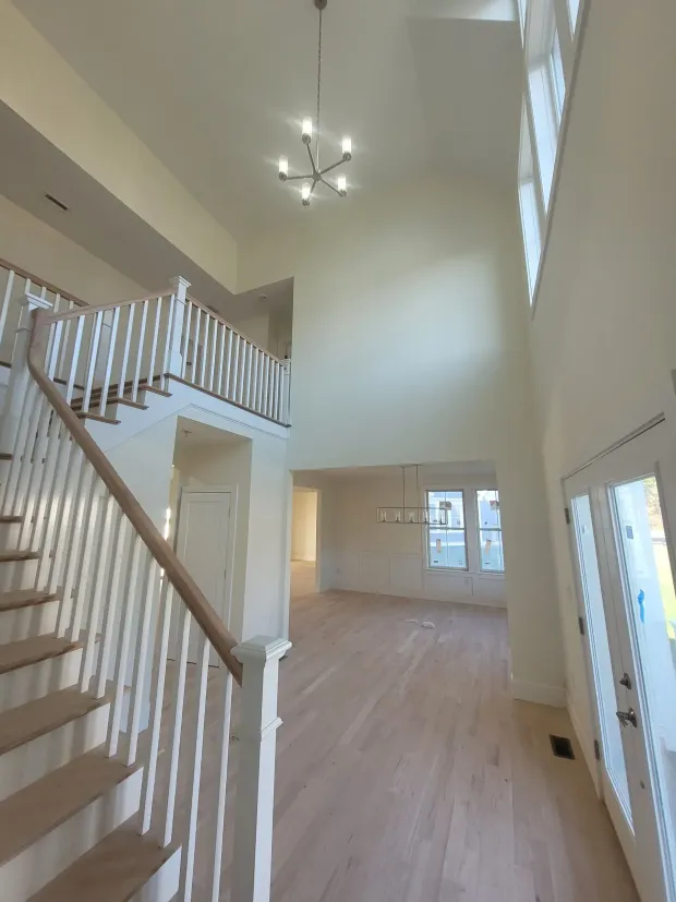 Grand entryway with staircase, high ceiling, chandelier, light hardwood floor, and large windows.