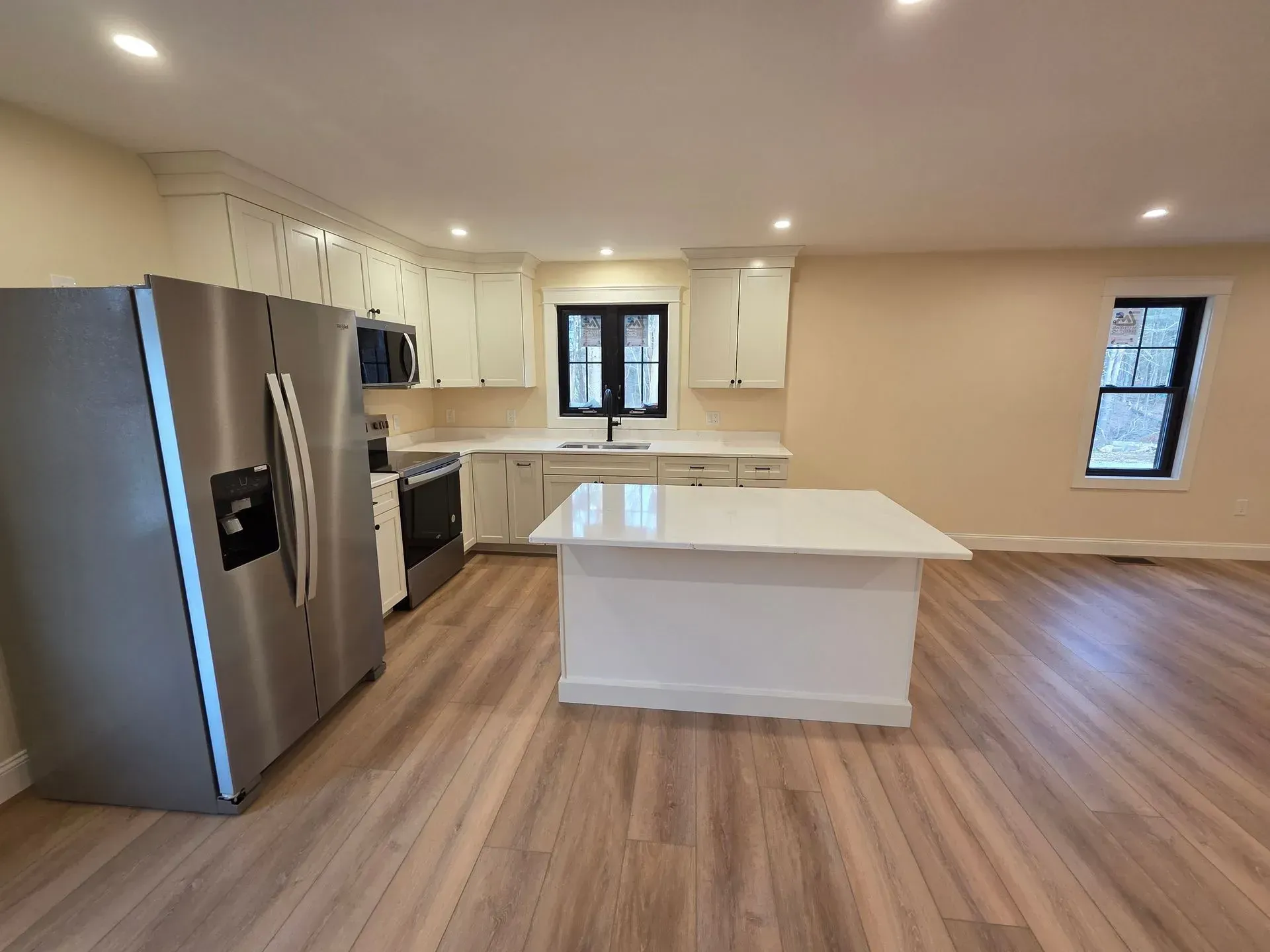 Modern kitchen with white cabinets, stainless steel appliances, and a white island on light wood floors.