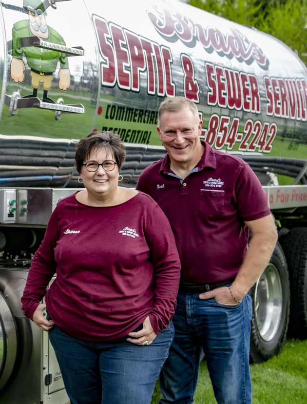 Two people in maroon shirts standing beside a service truck with a large company sign.