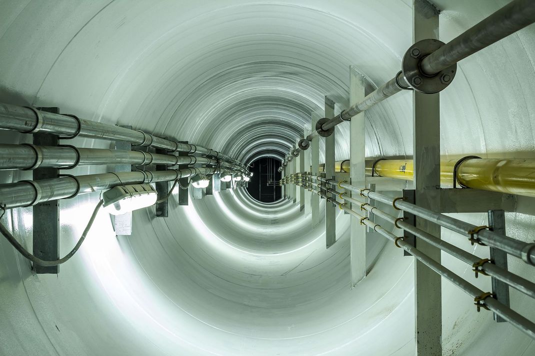 Long cylindrical industrial tunnel with pipes and cables running along the sides