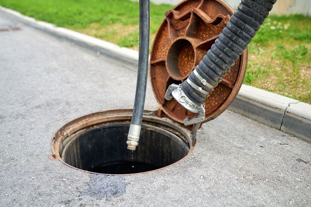 Close-up of a sewer manhole being cleaned with a vacuum hose on a street curb