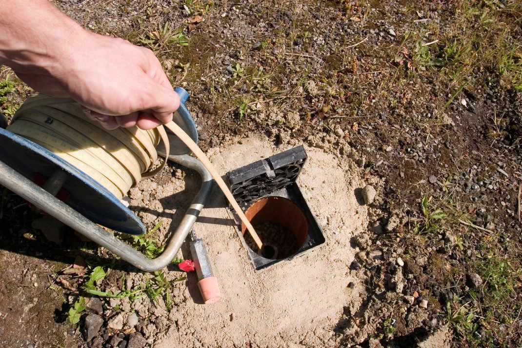 Hand holding a hose over an open utility pit in dry dirt