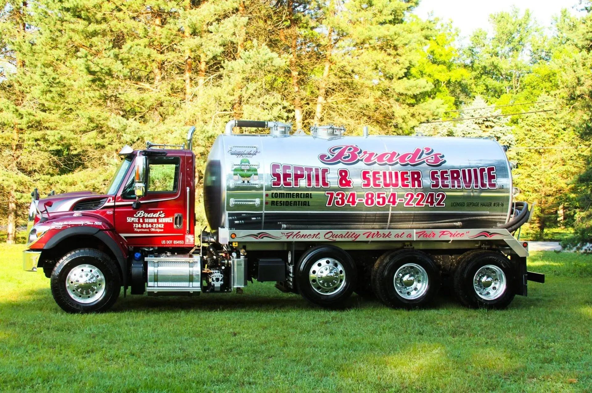 Red sewer service truck with silver tank parked on grass in front of trees