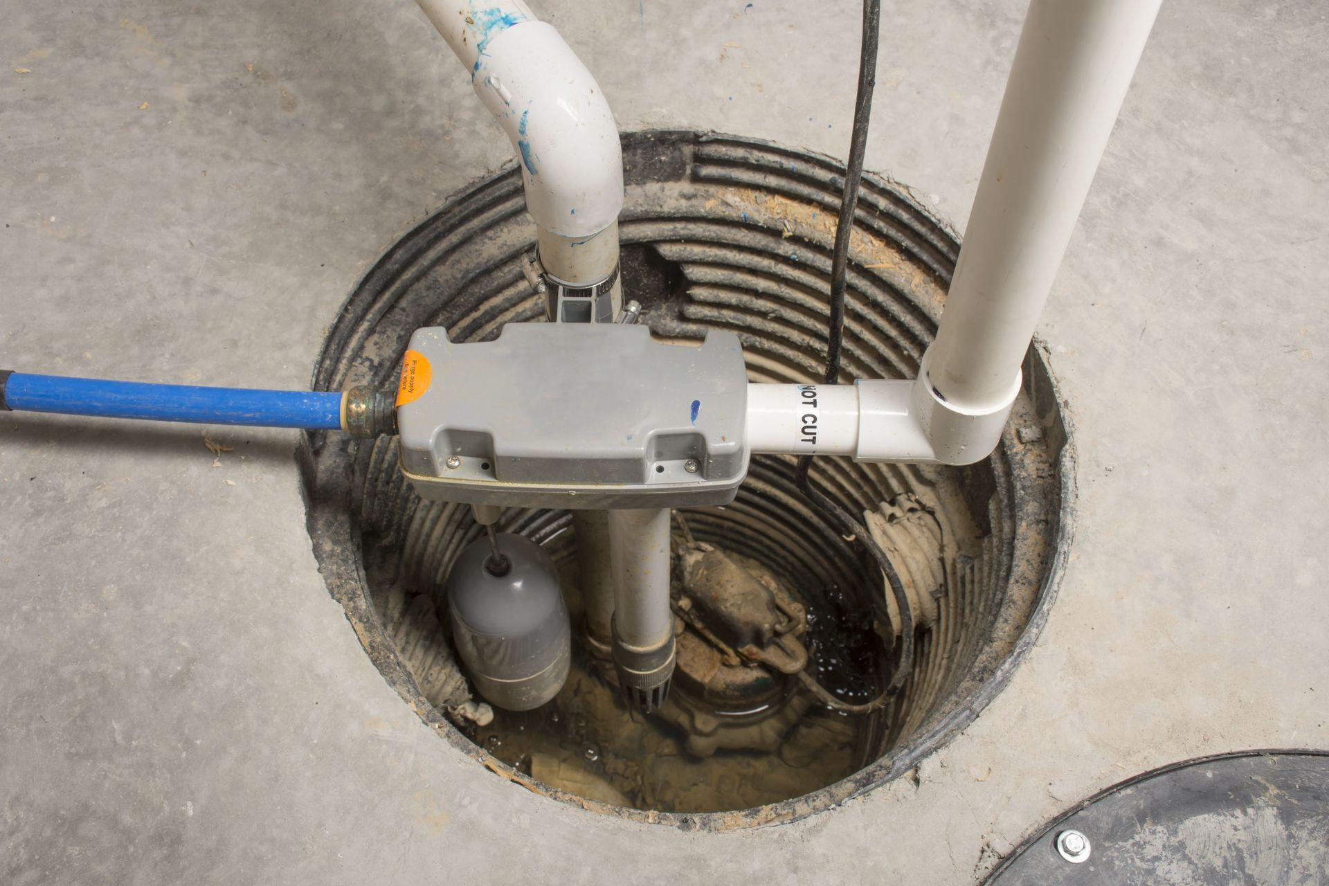 Open manhole with pipes, cables, and a pump assembly in concrete ground