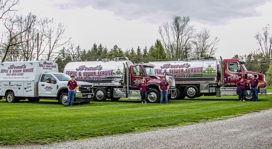 Four branded tanker trucks parked on grass, with drivers posing beside them under a cloudy sky.