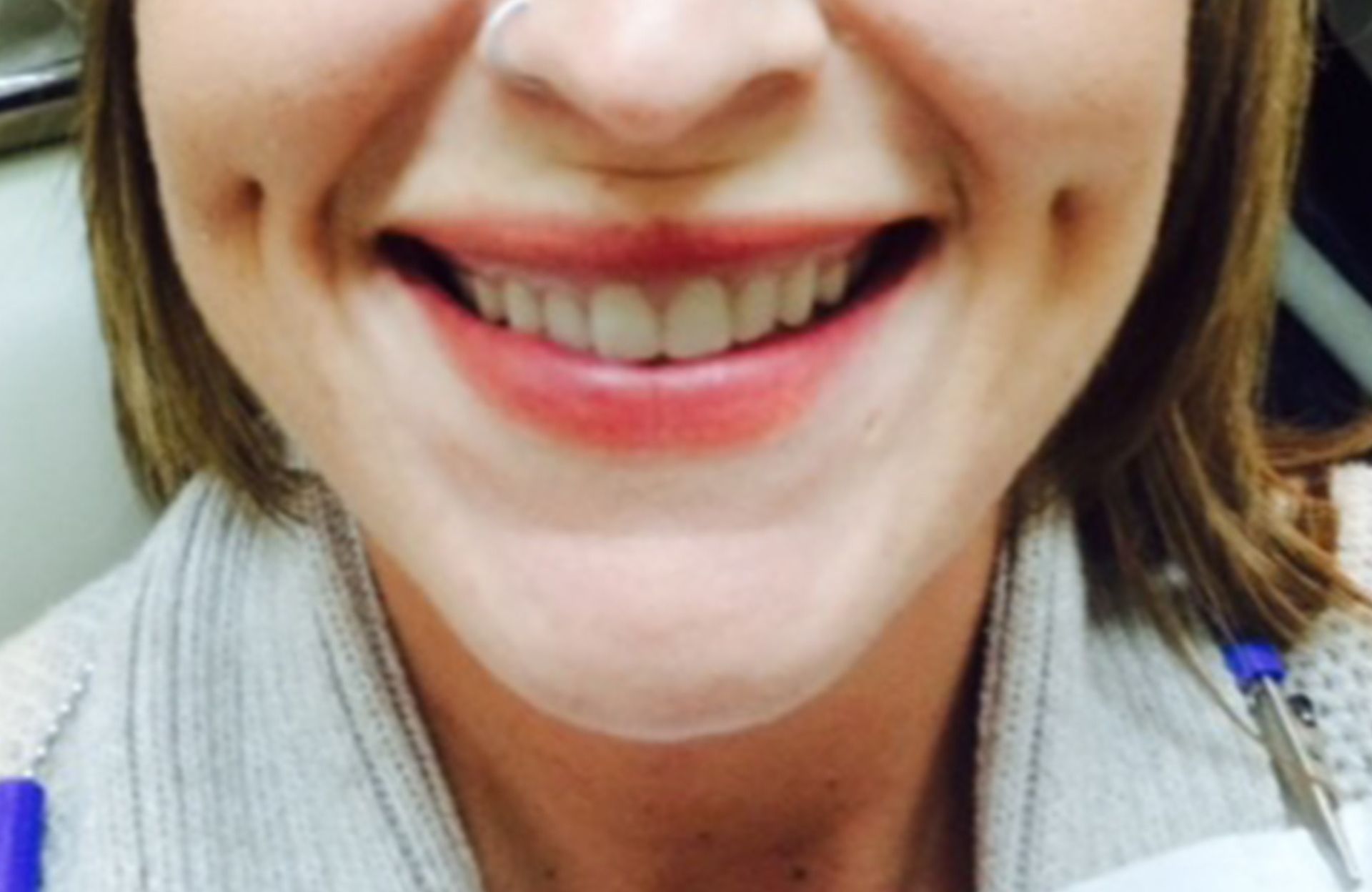 Close-up of a smiling person wearing a light gray scarf and blue earbud cables
