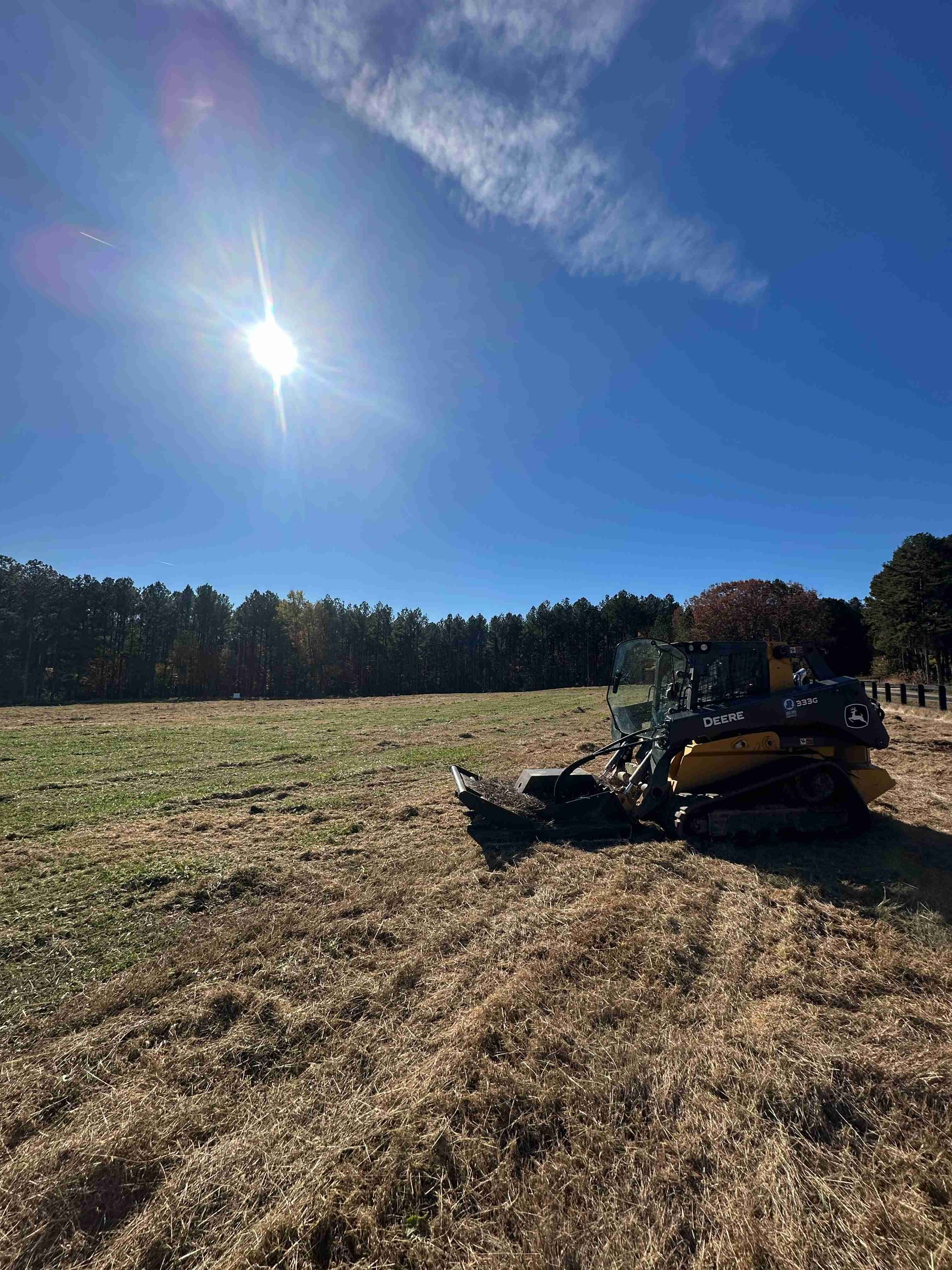 Harvester working in a dry field under a bright blue sky with the sun overhead