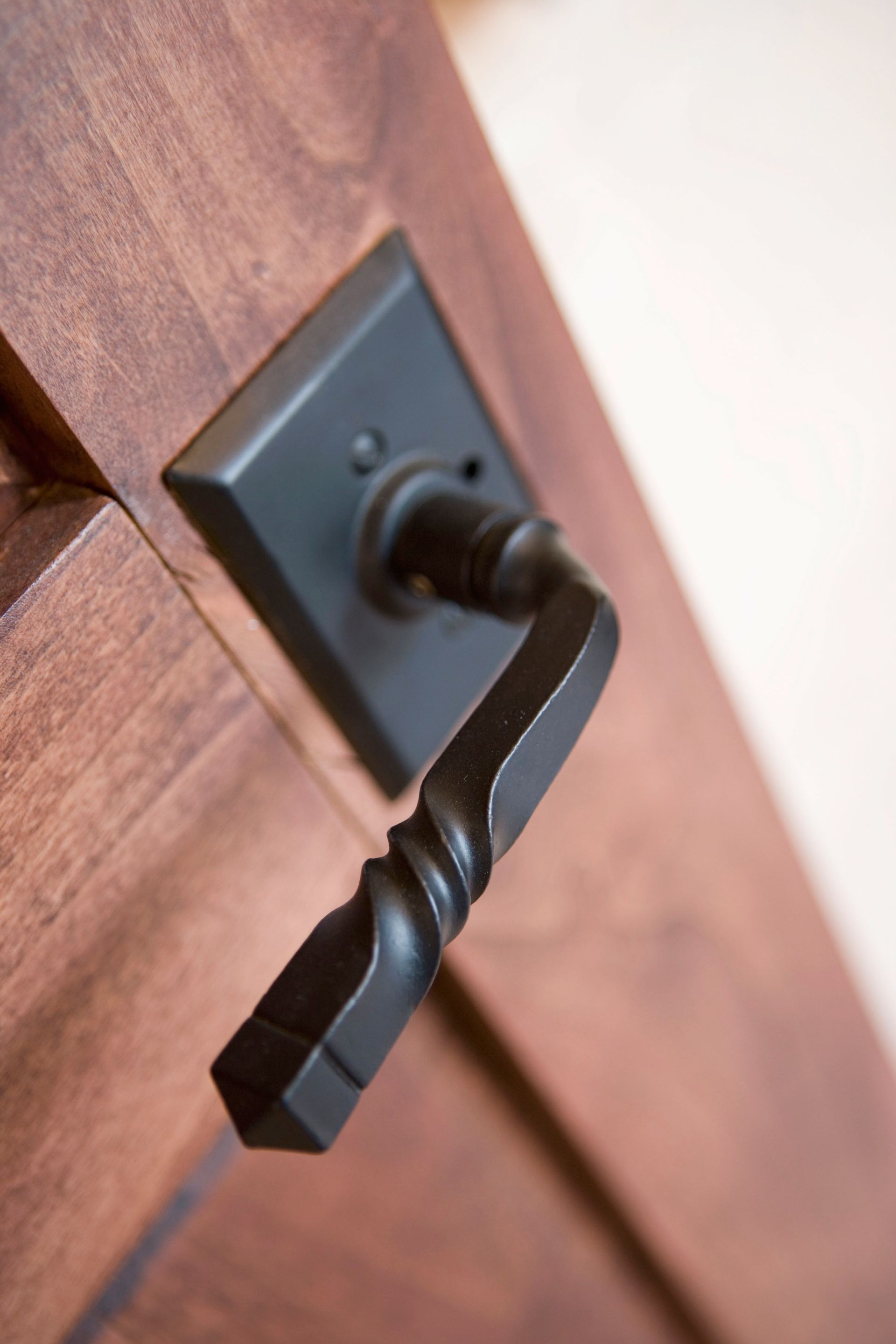 Black door handle on a wooden door, close-up. The handle is in a down position.