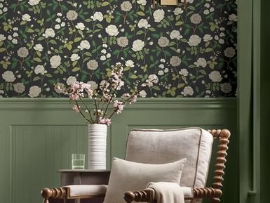 Room with floral wallpaper, green wainscoting, a wooden chair, and a vase of flowers.