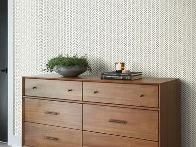 Wooden dresser with greenery and books in front of textured, cream-colored wallpaper.