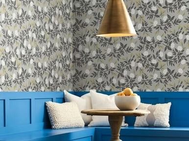 Blue booth seating with floral wallpaper, a small table, and a gold pendant light.