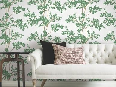 White tufted couch with black and patterned pillows against tree-patterned wallpaper.