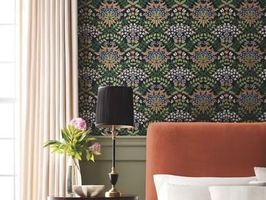 Bedroom with patterned wallpaper, curtains, lamp, and orange headboard.