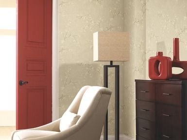 Red door, cream chair, lamp, and dark chest against textured beige walls.