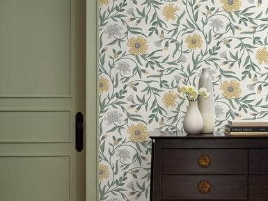 A room with floral wallpaper, green door, dark chest of drawers, and vases.