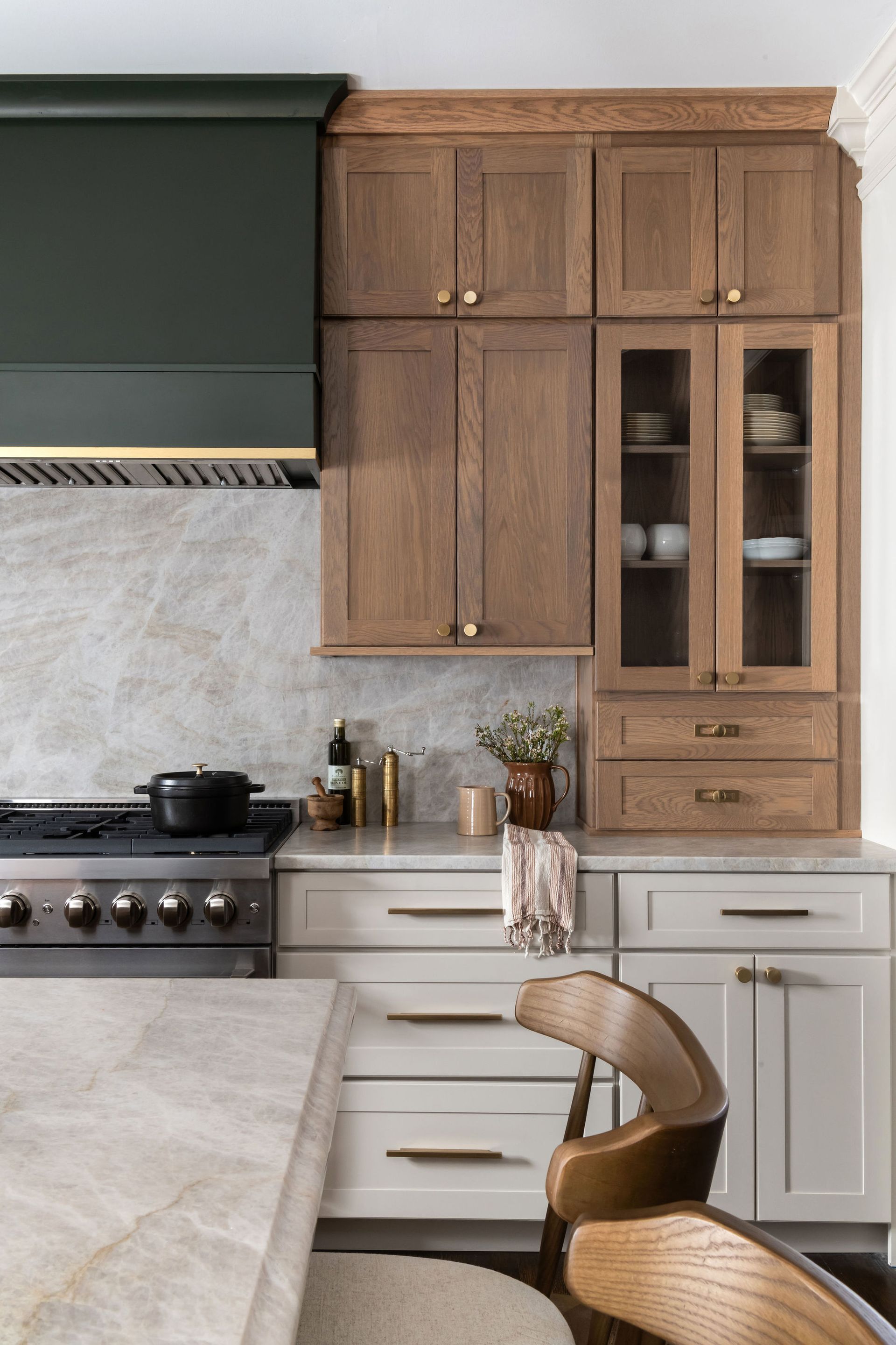 Kitchen with dark green range hood, light cabinets, and marble backsplash. A wooden chair is in the foreground.