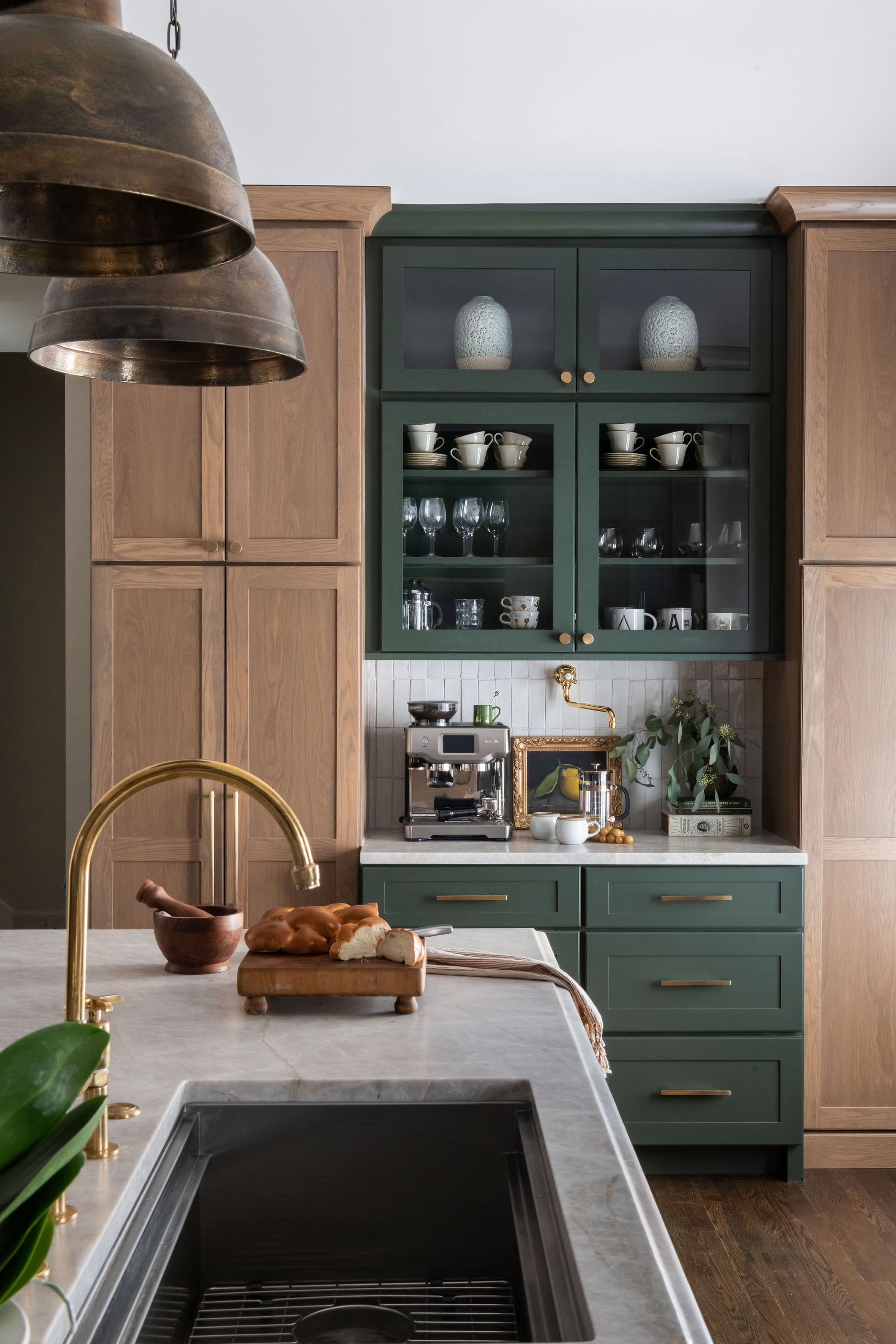 Kitchen with olive green and wood cabinets, gold faucet, and marble countertop.