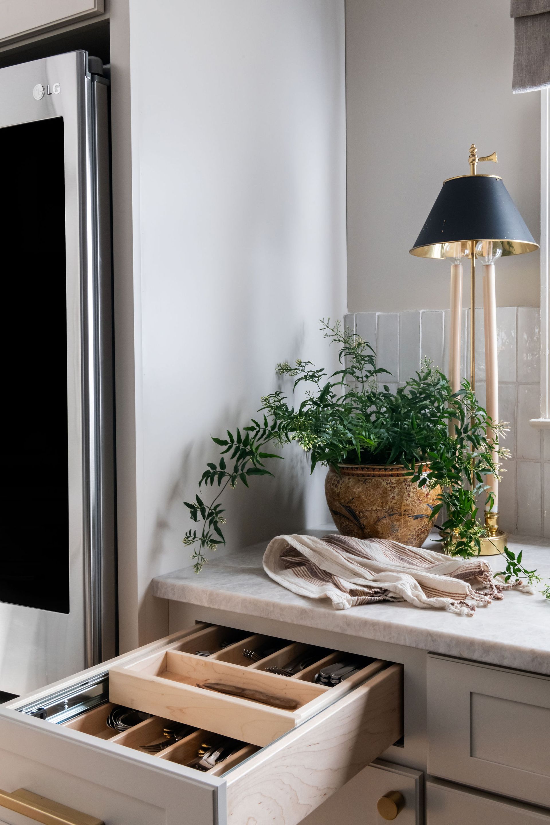 Kitchen countertop with a plant, lamp, and open drawer holding silverware.