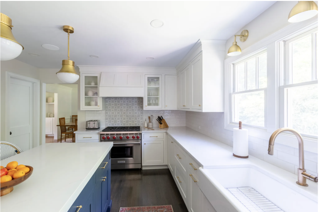 Kitchen with white cabinets, blue island, and gold light fixtures.