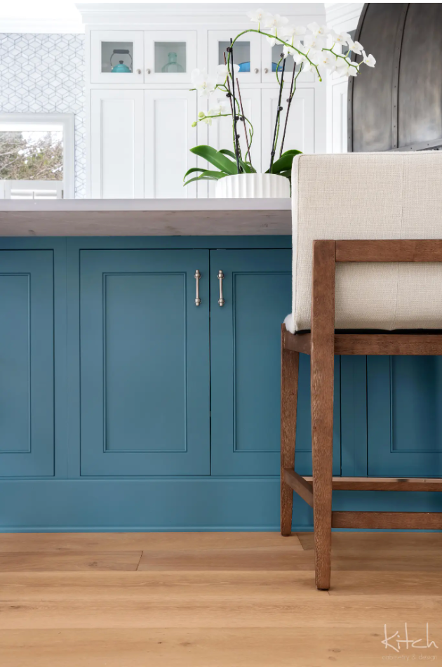Blue kitchen cabinets with silver handles and light wood floors, a bar stool with a white cushion.