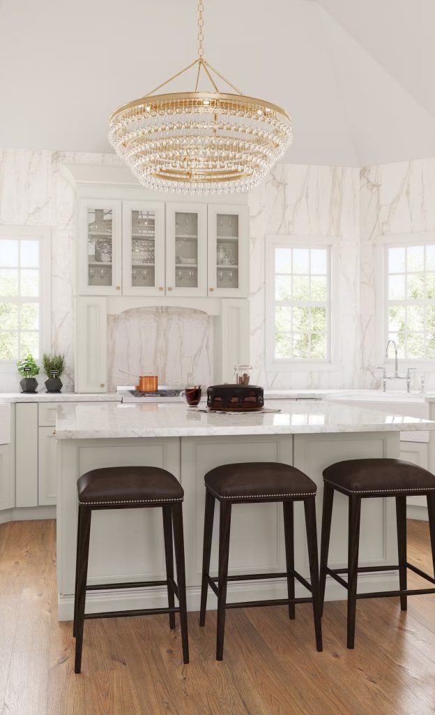 Kitchen with white marble island and cabinets, brown stools, and a gold chandelier.