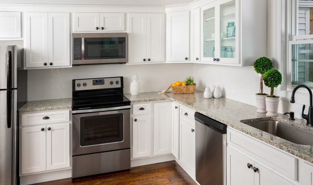 White kitchen with stainless steel appliances, granite countertops, and wooden floors.