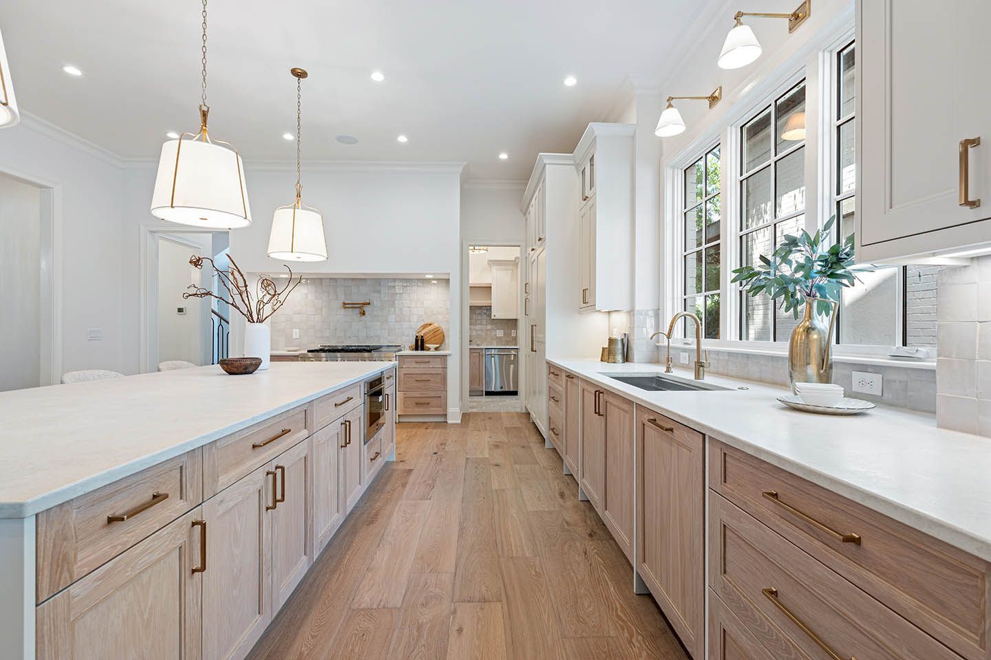 Bright white kitchen with light wood cabinets, long island, and a window above the sink.