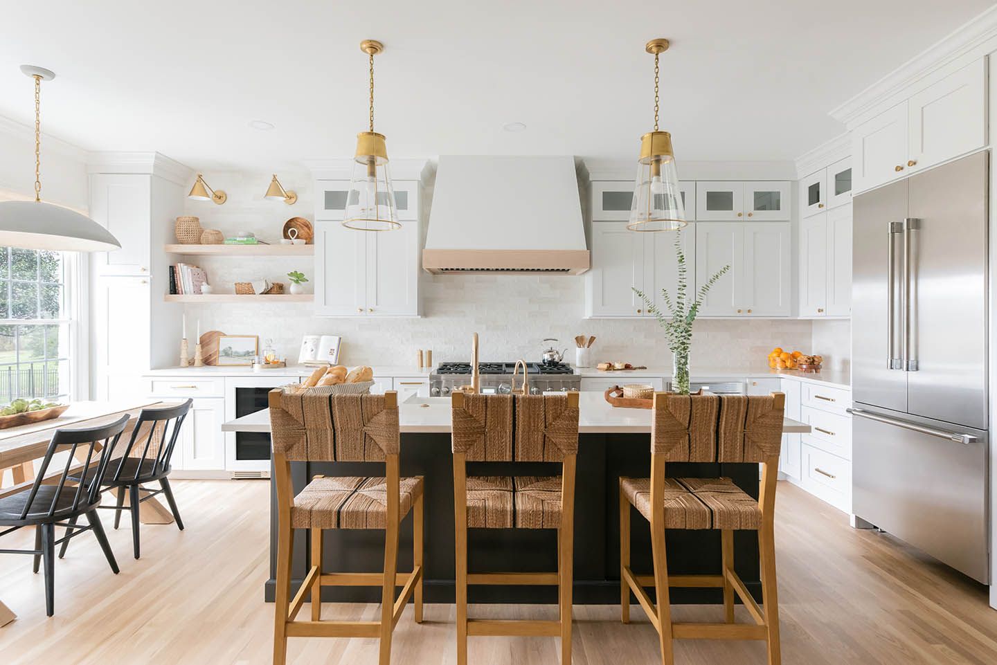 Modern kitchen with white cabinets, dark island, gold accents, and wooden bar stools.