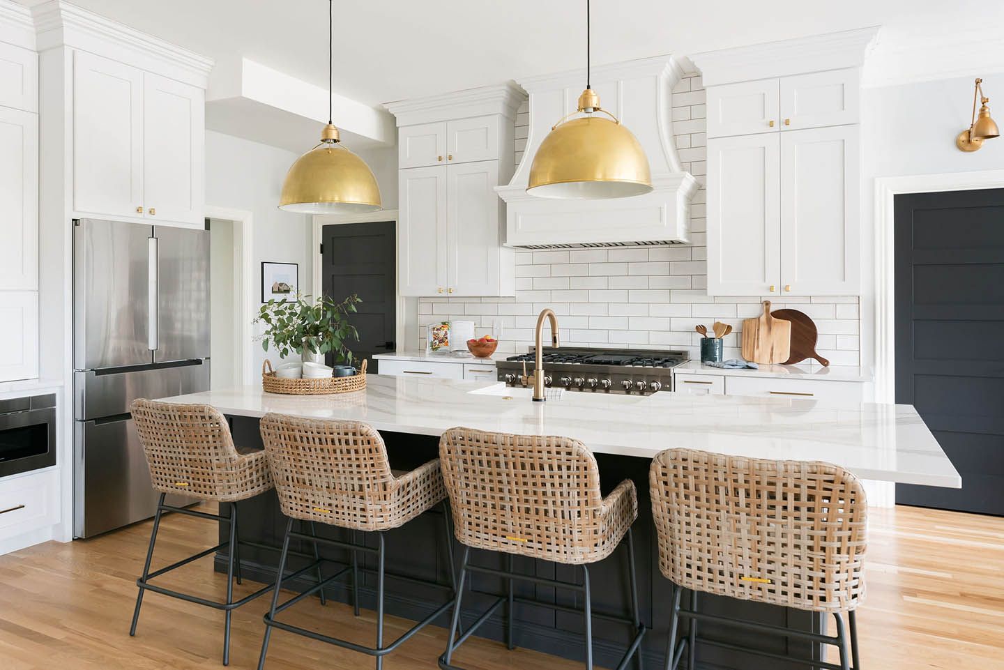 Modern kitchen with white cabinets, dark island, gold light fixtures, and woven bar stools.
