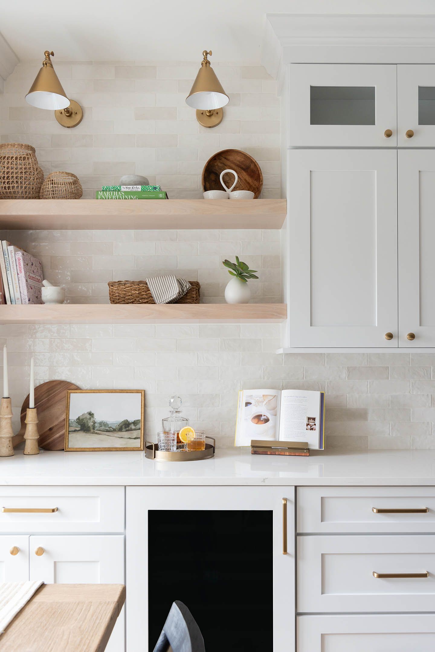 White kitchen with floating shelves, white cabinets, gold hardware, and wall sconces.