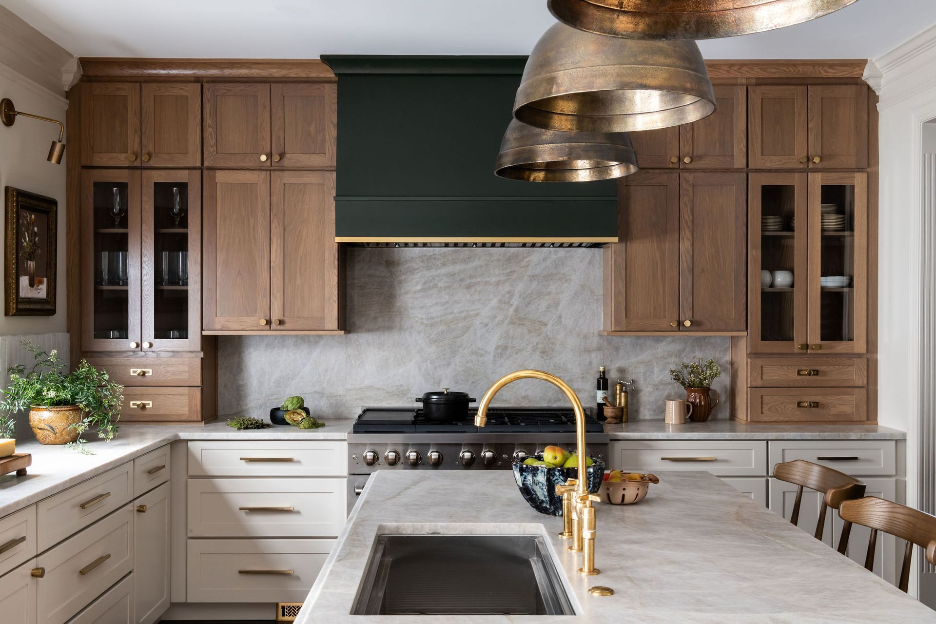 Kitchen with light countertops, wood cabinets, dark green range hood, and gold light fixtures.